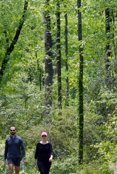 Two people walking on a greenway surrounded by trees